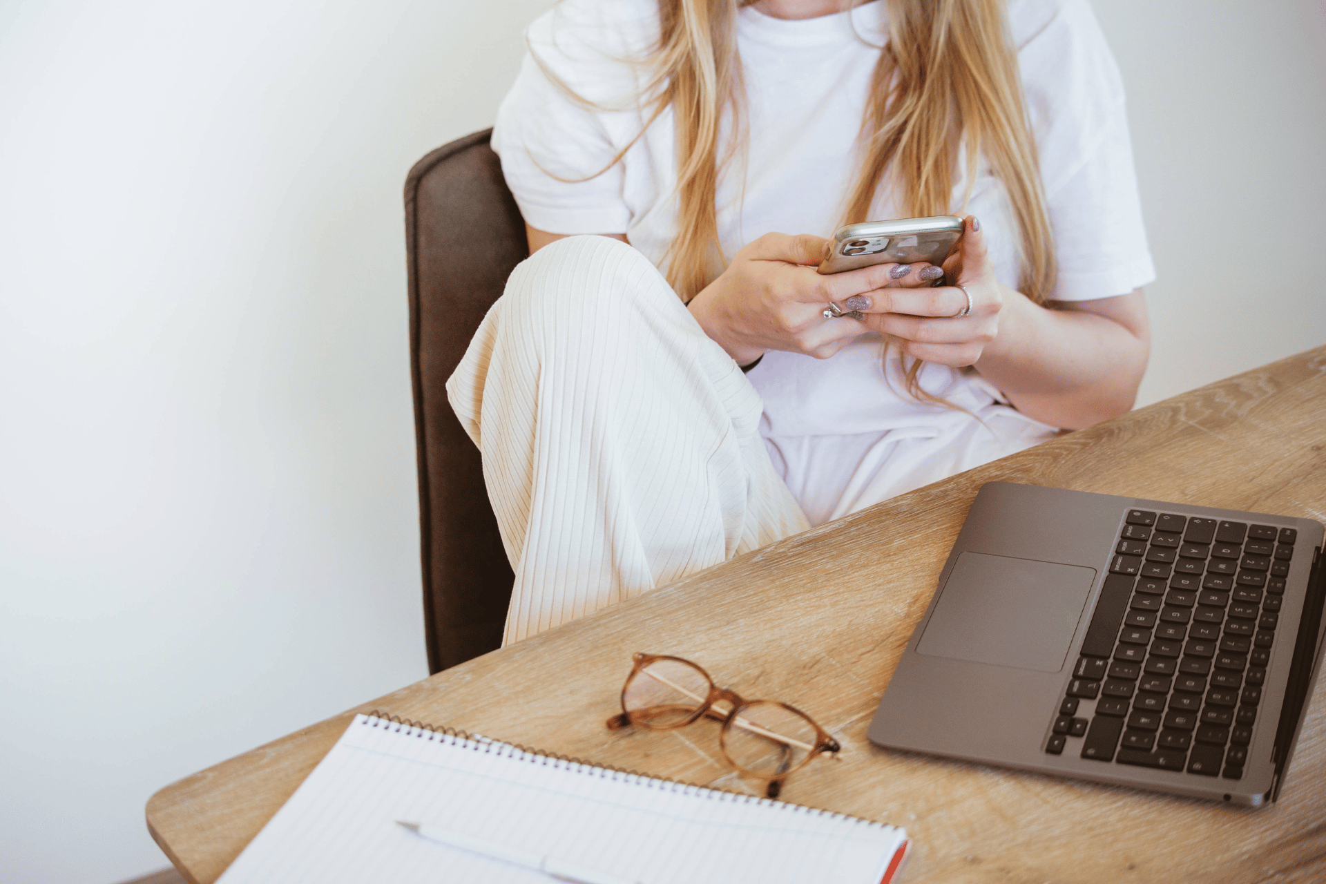 woman wearing a white t-shirt, cream pants on her phone with a computer