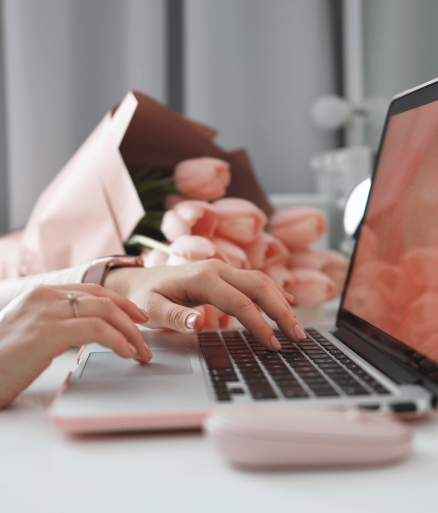 womens hands typing on computer with pink tulips in background